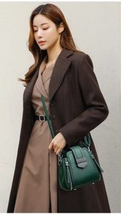 Detail view of dark green bucket bag with metallic zippers and trapezoid buckle