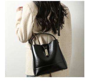 Detailed view of black leather bucket bag with gold buckle on model shoulder
