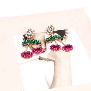 Detailed close-up of gold alloy cherry earrings with pink pearls and green rhinestones