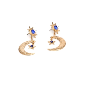 Boucles d'oreilles asymétriques étoile et lune dorées avec cristaux bleus sur fond blanc