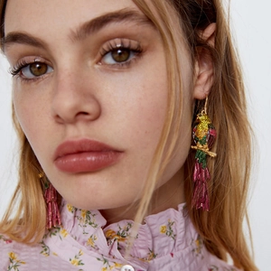 Boucles d'oreilles perroquet avec strass colorés et franges roses portées par modèle
