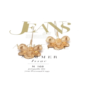 Macro detail of matte gold oversized flower drop earrings with textured petal layers