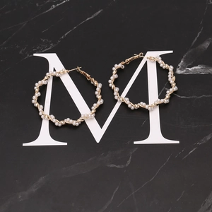 Chunky gold wire hoop earrings wrapped with white pearls on a dark marble surface