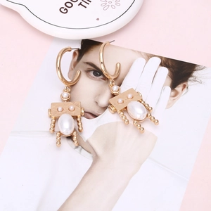 Minimalist gold robot earrings with pearl accents displayed on a fashion magazine