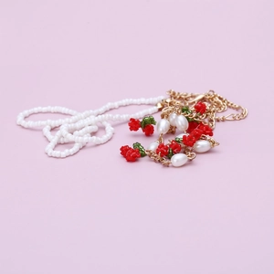 Handmade beaded necklace with white pearls and red cherry charms on pink background