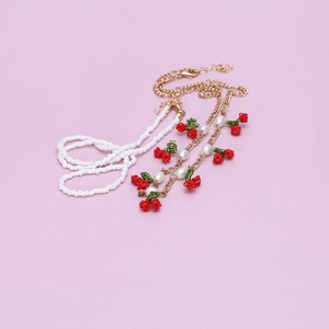 Detail view of a handmade beaded cherry necklace set with pearls on a purple backdrop