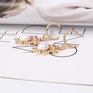 Gold robot-shaped drop earrings with pearls on a magazine background, 45-degree angle
