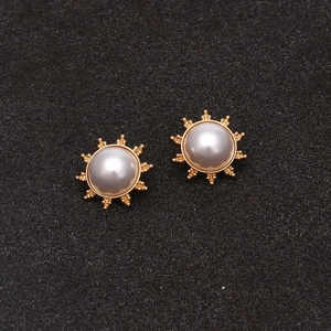 Vue détaillée des boucles d'oreilles soleil dorées avec perles blanches sur fond noir