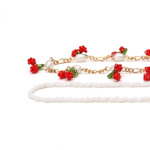 Detailed close-up of handmade beaded cherry pendants on a gold chain with white pearls