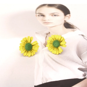 Detail shot of daisy stud earrings with yellow petals and green centers on art background