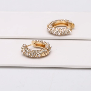Détail de boucles d'oreilles en U dorées avec strass pavés et petites perles blanches