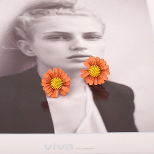 Detailed view of vibrant orange daisy stud earrings with yellow centers on artistic backdrop