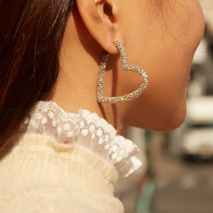 Élégantes boucles d'oreilles créoles cœur dorées avec strass brillants portées par un mannequin