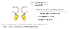 Detail showing handmade C-shaped pearl earrings with yellow beaded fruit and green leaf accents