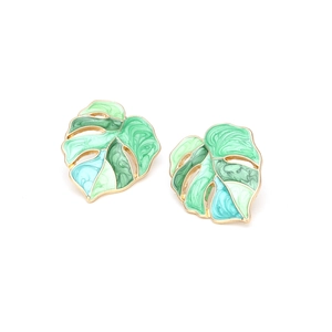 Close-up of monstera leaf earrings with green and blue enamel details in gold finish