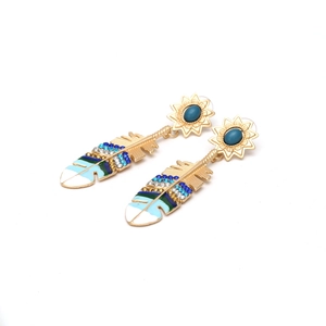 Detailed close-up of gold feather earrings with blue enamel and sparkling rhinestones