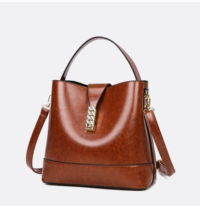 Close-up of brown oiled leather bucket bag with gold geometric metal lock and top handle
