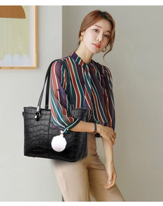 Detail of black embossed stone pattern tote bag with a white plush pompom charm