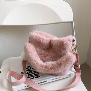 Chic pink faux fur bucket bag with woven strap and white pompom on a white chair