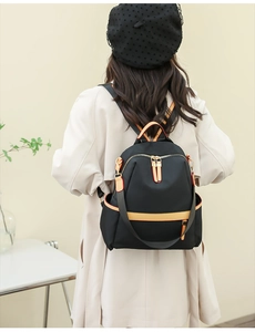 Detail of black nylon backpack with orange leather trim and dual zipper closure