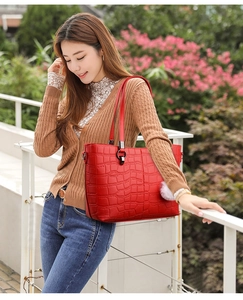 Detail of red croc-embossed tote bag with white plush ball charm in a lifestyle setting