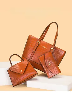 Dreiteiliges Set aus orangefarbener Krokoprägung-Tasche und Handtasche auf Steinpodest