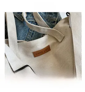Detail of cream canvas tote showing the brown leather label with embossed EARE LIFE text