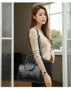 Detail view of a black crocodile-patterned handbag with V-shaped flap and top handle
