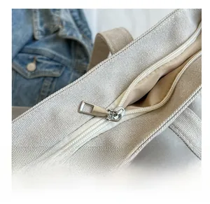 Detail view of the smooth silver metal zipper on an off-white canvas tote bag
