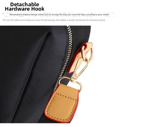 Detail of detachable gold-tone metal hook with brown leather strap on black nylon backpack