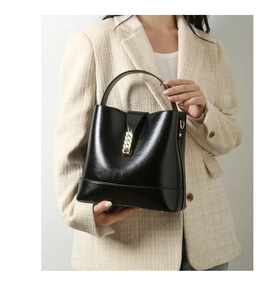 Detailed view of black patent leather tote bag with gold metal buckle on tweed blazer