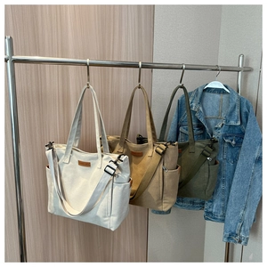 Detail of canvas tote bags in cream, khaki, and green with adjustable straps and side pockets