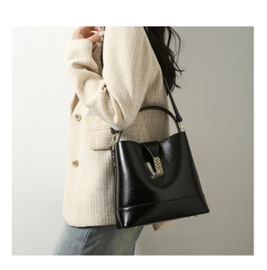 Side view of black leather bucket bag with gold buckle on model in cream blazer