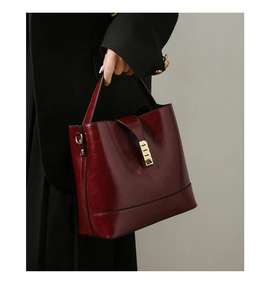 Detail of wine red bucket bag in oil wax leather with gold buckle held by a model