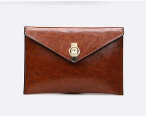 Close-up of brown leather envelope clutch bag with gold round buckle and oil wax texture