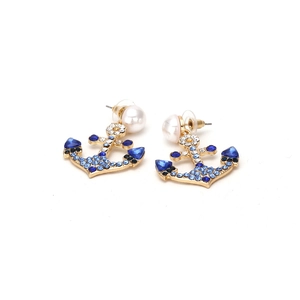 Detail of anchor earrings with blue crystals and pearls on polished gold metal