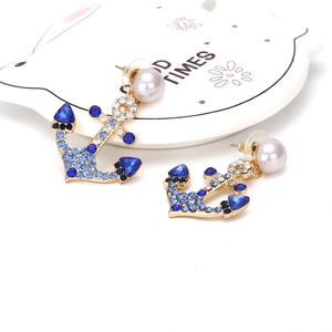 Close-up of gold anchor earrings with blue rhinestones and a white pearl accent