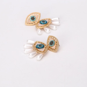 Detail of evil eye earrings with blue rhinestones and dangling white pearl drops