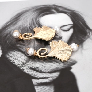 Gouden ginkgo blad oorbellen met parels gepresenteerd op een vintage tijdschrift