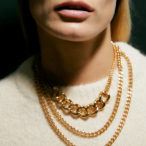 Layered gold curb chain necklace set featuring multiple strands on a white sweater