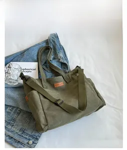 Detail view of dark green canvas tote bag with brown leather logo and metal hooks