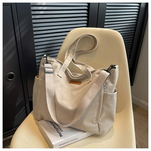 Detail of off-white canvas tote bag with adjustable strap and side pocket on a chair