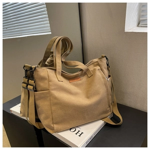 Detail of khaki canvas tote bag with leather logo patch and adjustable shoulder strap