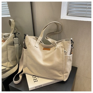 Detail of minimalist cream canvas tote bag featuring adjustable strap and logo patch