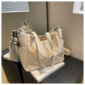Detail of beige canvas tote bag with brown leather label and functional side pocket