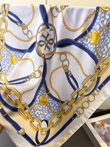 Detailed view of silk scarf featuring gold chains, blue belt patterns and heart pendants