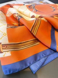 Detailed view of luxury orange silk scarf featuring equestrian chain prints and leather straps