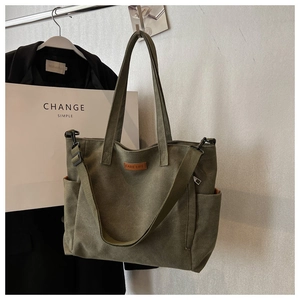 Detail of army green canvas tote bag featuring leather logo tag and wide shoulder strap