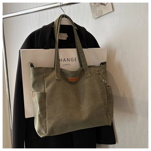 Detail of olive green canvas tote bag with side pockets and brown leather brand patch