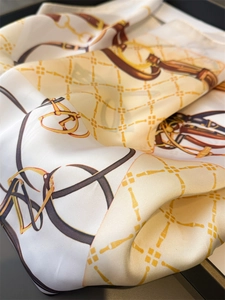 Detailed close-up of luxury faux silk scarf with gold chain and horsebit equestrian print